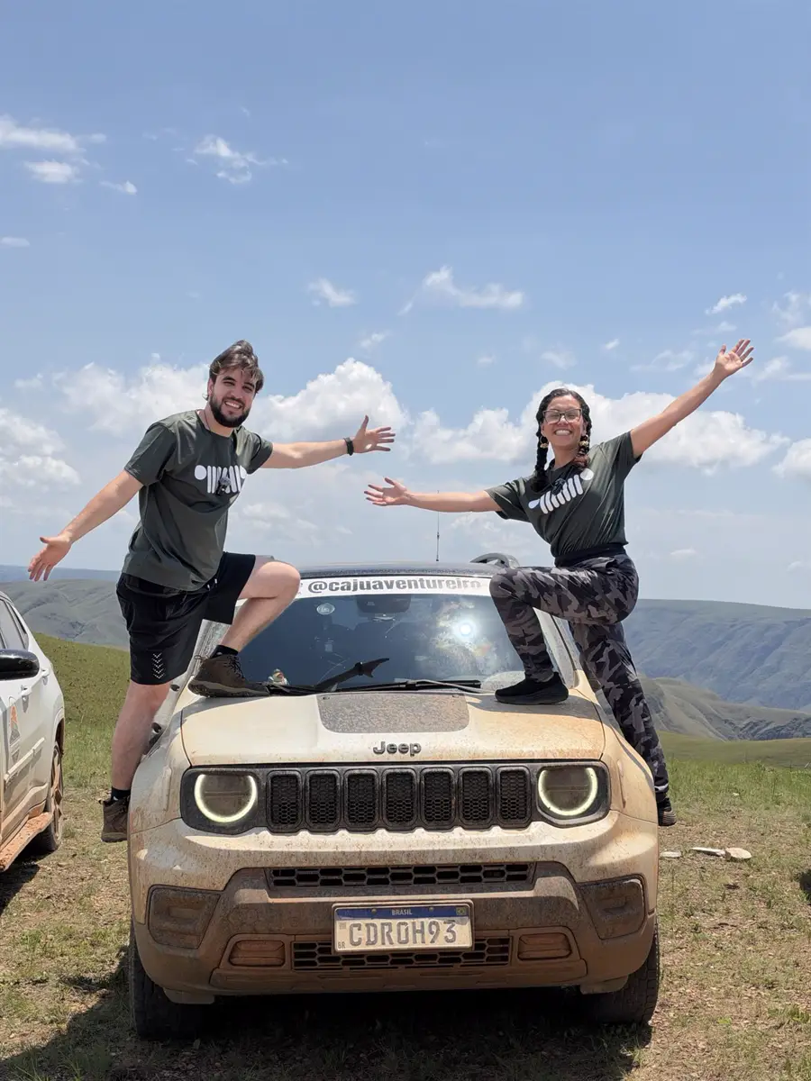 Julio e Cauana de braços abertos em cima do Jeep sujo de barro, no alto da serra